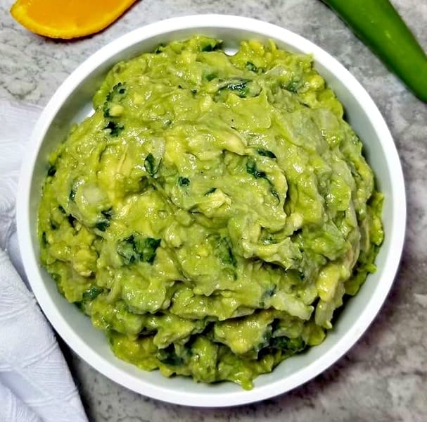 Best Homemade Guacamole in a white bowl with an orange and serrano pepper